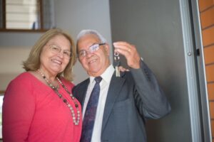 Senior man and woman smiling holding up keys to a new home