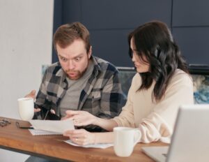 An adult child and an older parent (or two adult siblings) sitting together at a kitchen table with paperwork