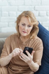 Woman in her 60s pausing to check a text on her phone, a key habit for avoiding scams targeting seniors